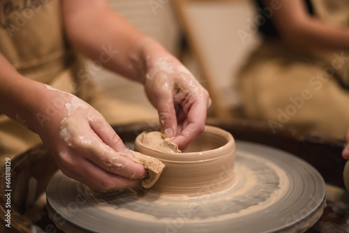 Potter girl works on potter's wheel, making ceramic pot out of clay in pottery workshop. Art and hobby concept