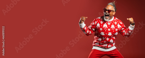 Ugly Christmas Sweater Day. Cool old man dancing in knitted clothes and glasses, red background. Banner, copy space