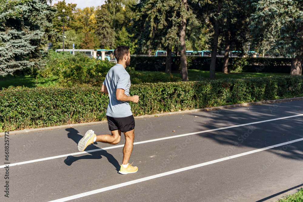 Obraz premium Warm-up running for an active workout, a young guy is an athlete. A man stretching his body outdoors taking care of his health.