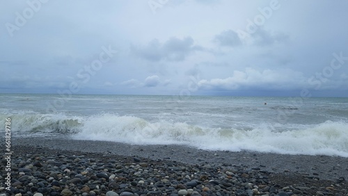 Gray pre-storm sea with the shore rolling on black wet pebbles and gray clouds above it