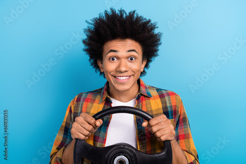 Portrait of satisfied positive guy with perming coiffure dressed plaid shirt hands hold steering wheel isolated on blue color background