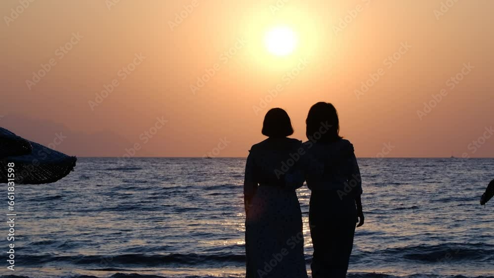 silhouette of two women hugging and walking on the beach at sunset silhouette of two women hugging and walking on the beach at sunset