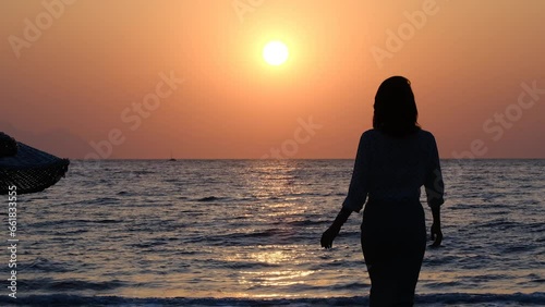 silhouette of woman walking alone on the beach at sunset