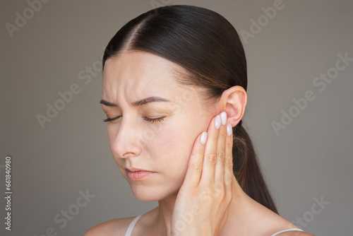 a young woman is in pain, closing her eyes, pressing her palm to her ear, suffering from otitis. Deafness, ear inflammation.