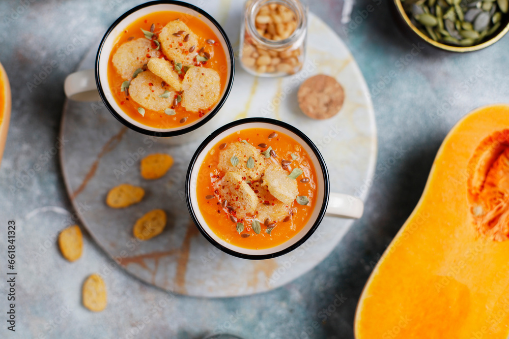 Roasted butternut squash soup with cream and pumpkin seeds on two white mugs. Roasted butternut squash soup with cream and pumpkin seeds on two white mugs.