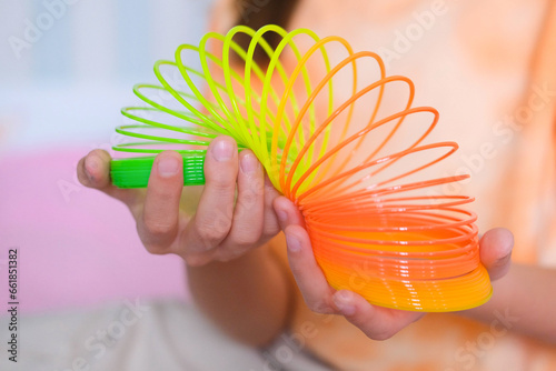 Child playing orange and green tight, colorful flexible children's toy, fun plastic toy. Teen girl plays slinky