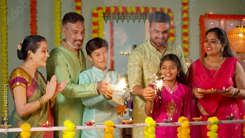 Group of family member enjoying by seeing kids playing with sparklers or fireworks during diwali festival celebration at home - concept of Happy Moments, traditional culture and reunion