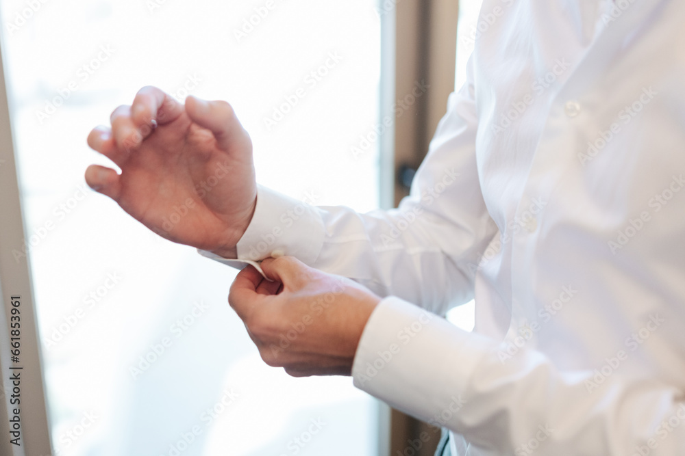 The groom holding his shirt cuffs, putting on cufflinks on his wedding day The groom holding his shirt cuffs, putting on cufflinks on his wedding day