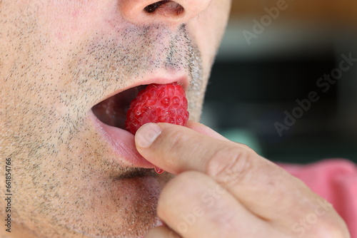 Close up of male face while bringing fresh, bright red raspberry to his mouth