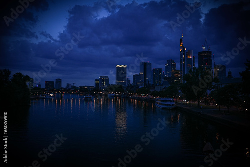the skyline in frankfurt am main at night. panorama picture from a bridge over a big river. main promenade and an excursion boat in the evening light