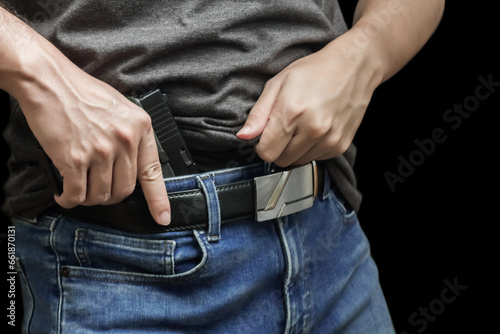 Hided handgun under the denim belt. a man in jeans and a t-shirt holds a gun in his hand from the back