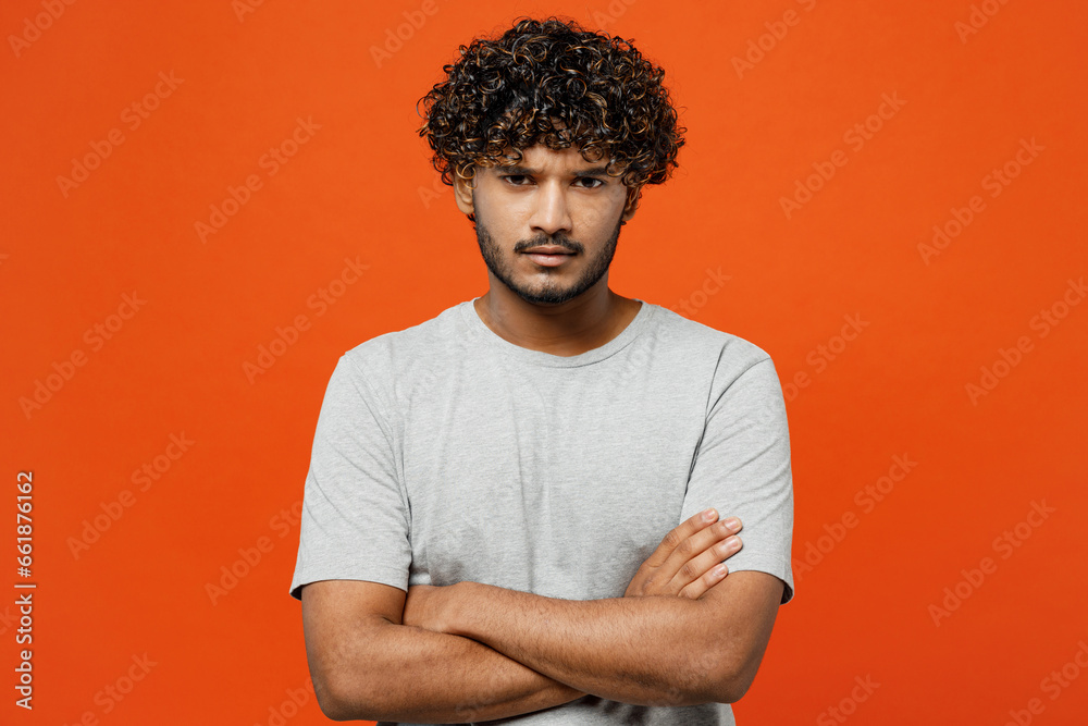 Φωτογραφία Young sad frowning mad furious shrewd Indian man he wearing t-shirt casual clothes hold hands crossed folded looking camera isolated on orange red color background studio portrait