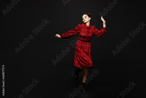 Full body cheerful fun young woman with Halloween makeup face art mask wear clown costume red dress dance raise up hands isolated on plain solid black background studio. Scary holiday party concept.