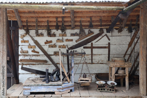 Collection of planers and retro wood saws hang on a wooden wall near an old house. Carpenters plane and other things on wall