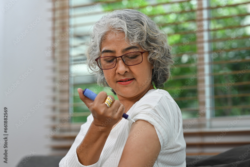 Portrait of a Diabetic mature woman taking an insulin shot on her arm. Diabetes and elderly health care concept - obrazy, fototapety, plakaty 