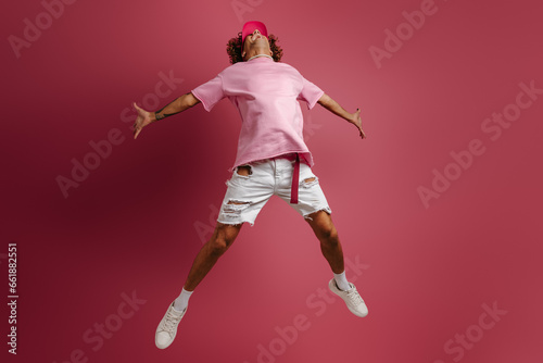 Full length of young fashionable man jumping against red background