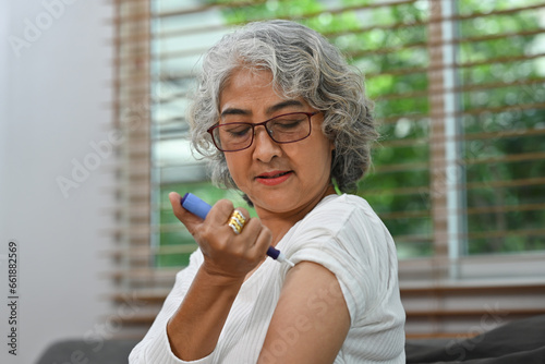 Portrait of a Diabetic mature woman taking an insulin shot on her arm. Diabetes and elderly health care concept photo