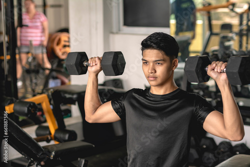 A young asian man looking focused while doing a set of seated dumbbell presses at the gym. Shoulder workout and training.