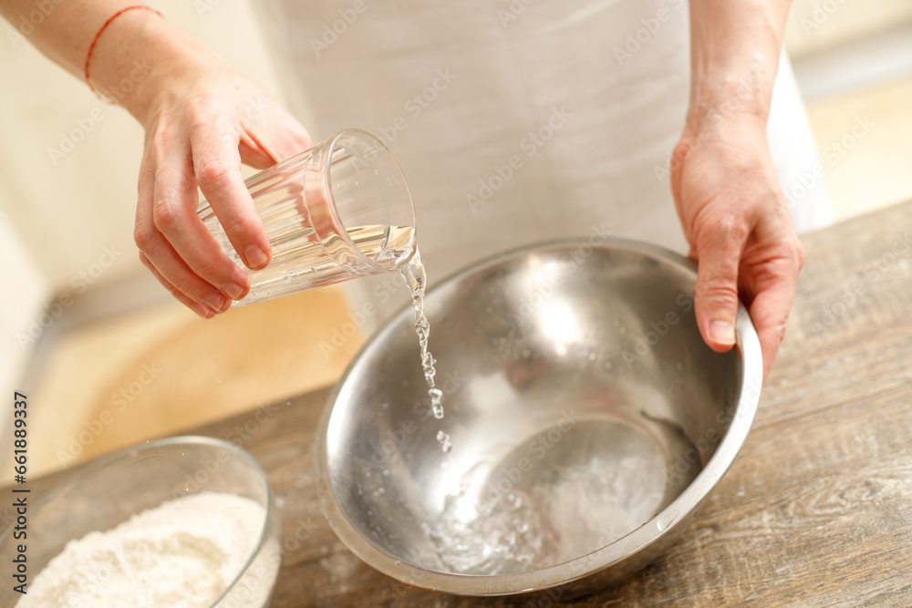 Fototapeta premium Young man kneading dough on wooden table. Males hands making bread on the kitchen. Baking concept.