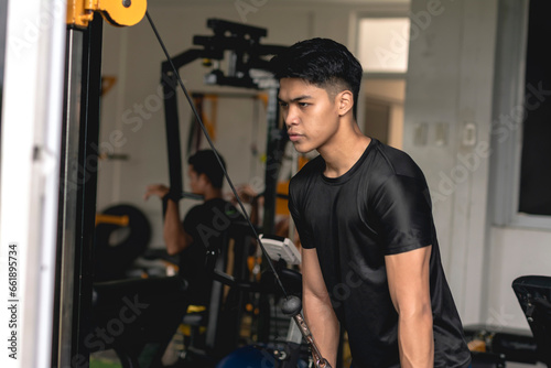 A young handsome asian man does a set of tricep rope pushdowns on the cable machine at the gym.