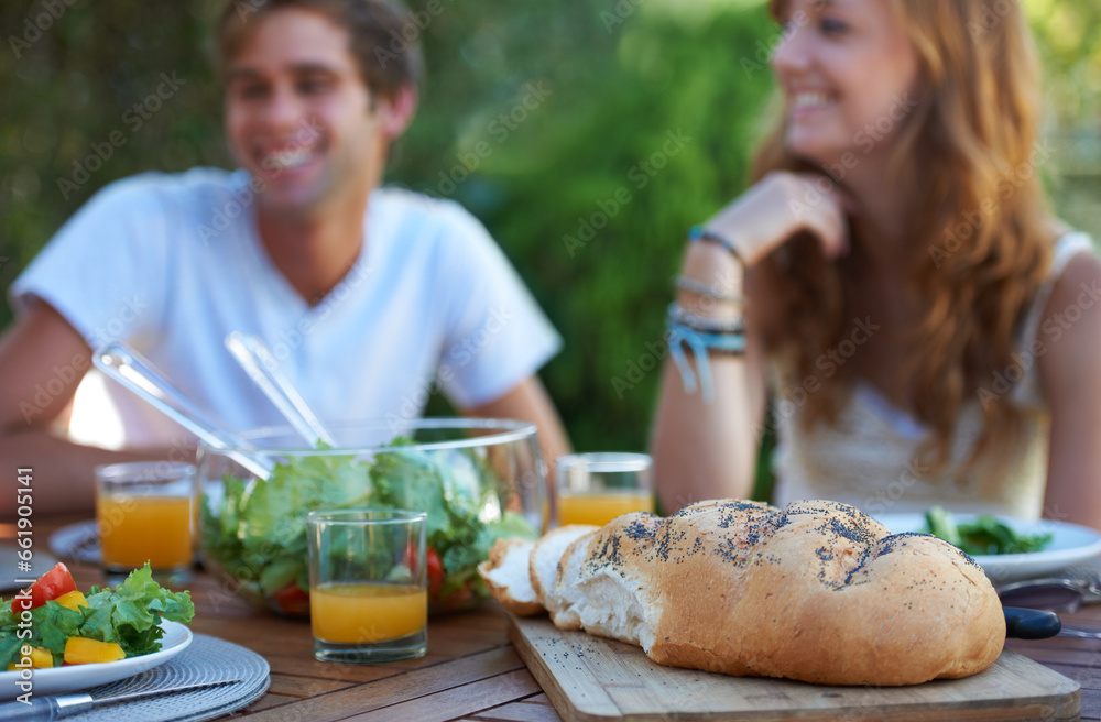 Friends, bread and food in backyard for lunch and appetizer with a smile and snacks. Salad, talking and young people outdoor of a home with drinks and funny joke together with in summer with meal