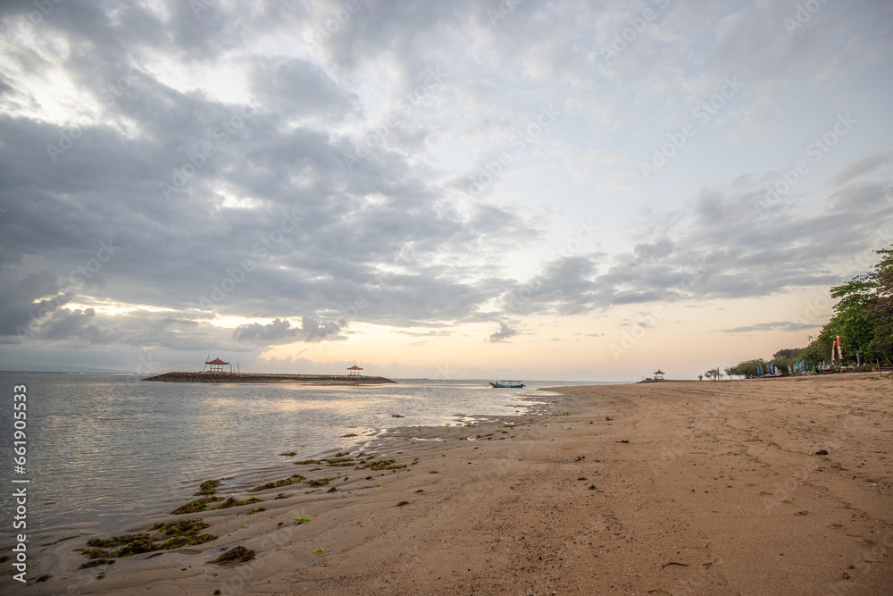 Beautiful sunrise on Sanur beach. Temple in the calm sea. Small waves in the morning. Sandy beach on the dream island of Bali. Sunset in a landscape shot, looking into the horizon