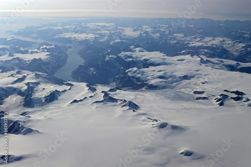 Aerial view of mountains, snow fields, crevasses and glaciers of southern Greenland from airplane window on clear sunny autumn day.