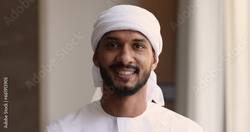 Close up head shot portrait young confident and ambitious Sudanese African business man wear traditional muslim white headscarf and thawb smiling looking at camera posing in office. Career, business