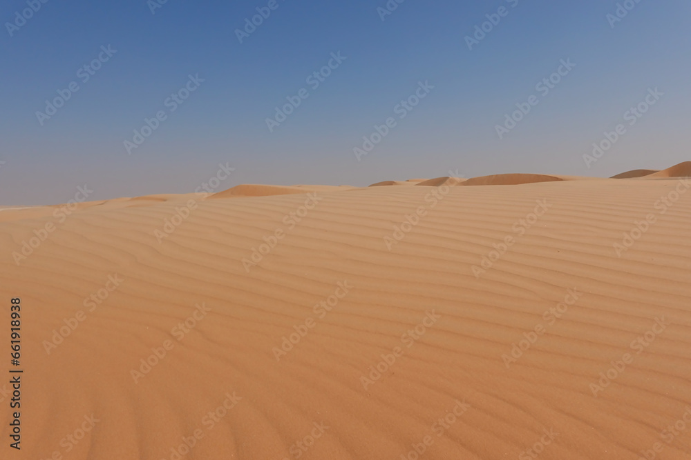 Shot from below golden desert sand and small dunes on the horizon and blue sky.