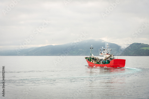 Fishing boat leaving the port of Getaria on a cloudy day with the mountains covered by the fog in the background, Gipuzkoa, Basque Country, Spain