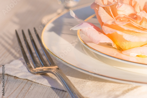 Romantic table setting  close up for salmon rose flower on the white plates  fork on the white napkin son sunlight