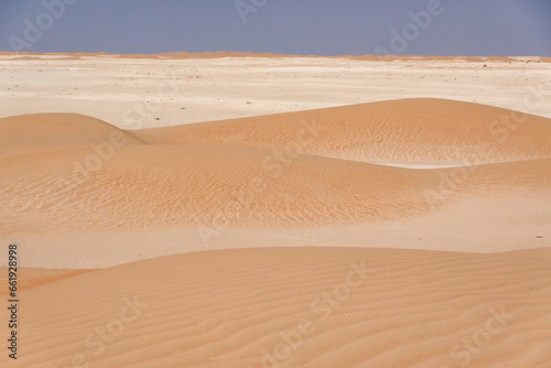 Panorama of small dunes with red sand and vertical streaks on the limestone horizon.