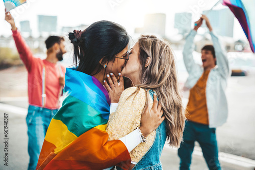 Diverse group of young people celebrating gay pride festival day - Lgbt community concept with two girls kissing outdoors - Multiracial trendy friends standing on a yellow background photo