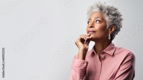 Portrait of pensive confident senior African American woman imagines something in her mind, looks upwards, being deep in thoughts, touching chin, isolated on white, copy space. photo