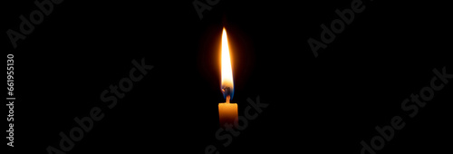 Single burning candle flame or light glowing on a small yellow candle on black or dark background on table in church for Christmas, funeral or memorial service with copy space.