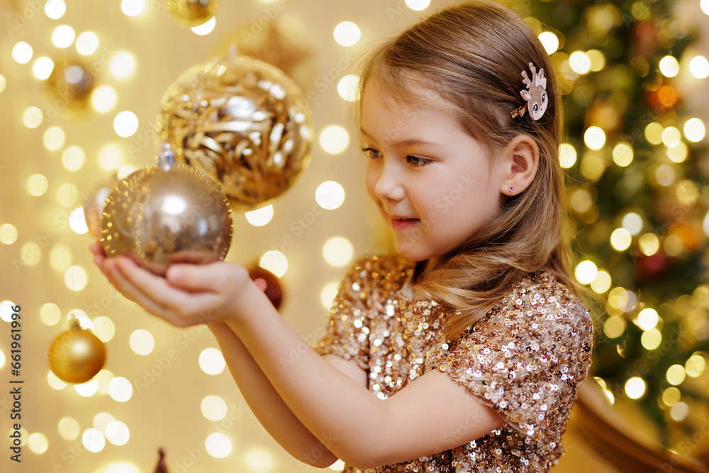 Naklejka premium Cute little girl holding golden christmas ball