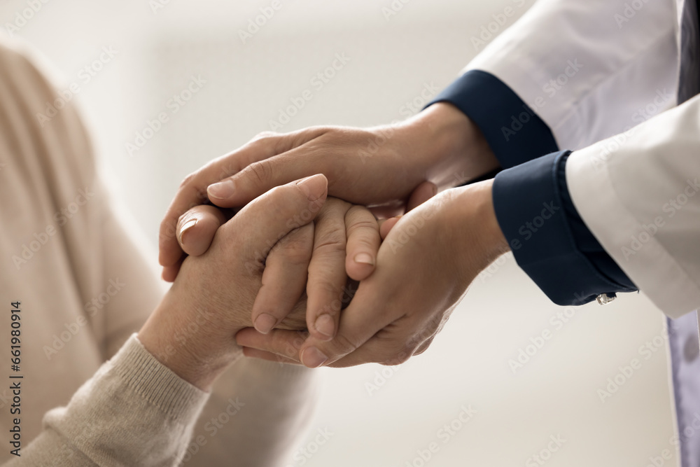 Fototapeta premium Close up of young medical worker holding hands older female patient, express hope and professional aid, psychological support. Sick senior lady receiving empathy compassion of physician. Health care