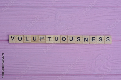 word voluptuousness from small gray wooden letters lies on a pink wooden table

