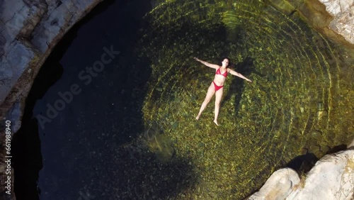 Overhead aerial view of a natural water pool with a woman in a bikini floating. Mountain environment with water, trees and rocks. photo