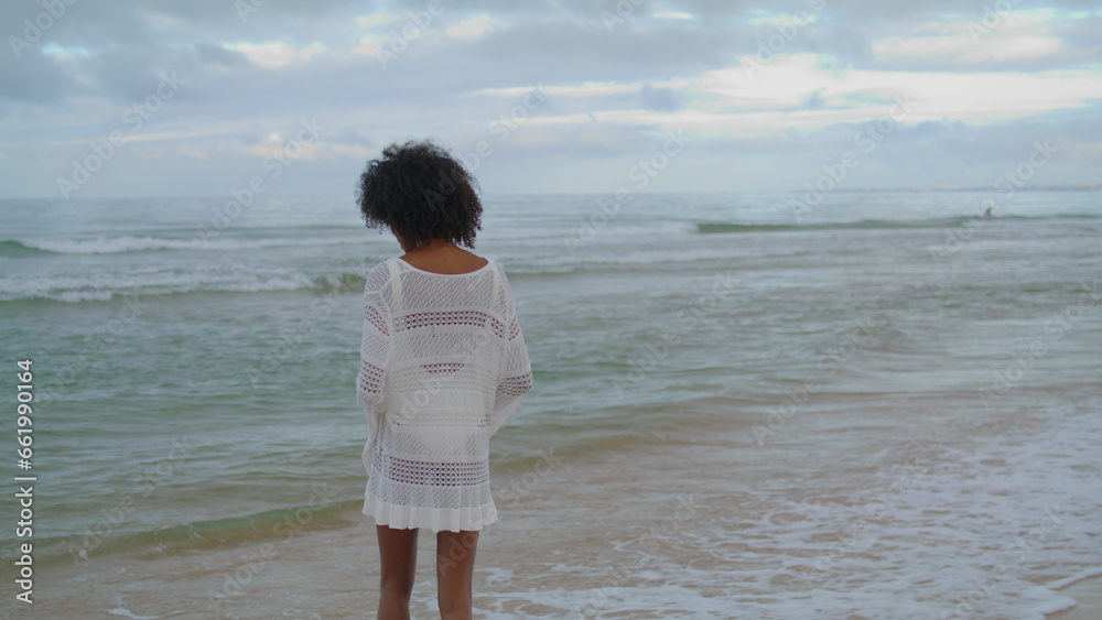Woman contemplating ocean beach in white outfit. Curly slim girl looking sea Woman contemplating ocean beach in white outfit. Curly slim girl looking sea