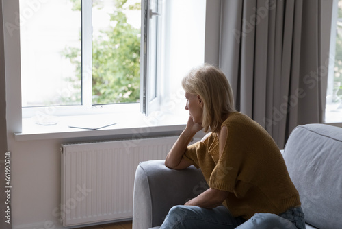 Canvas Print Depressed lonely middle aged woman looking at open window, sitting on couch at h