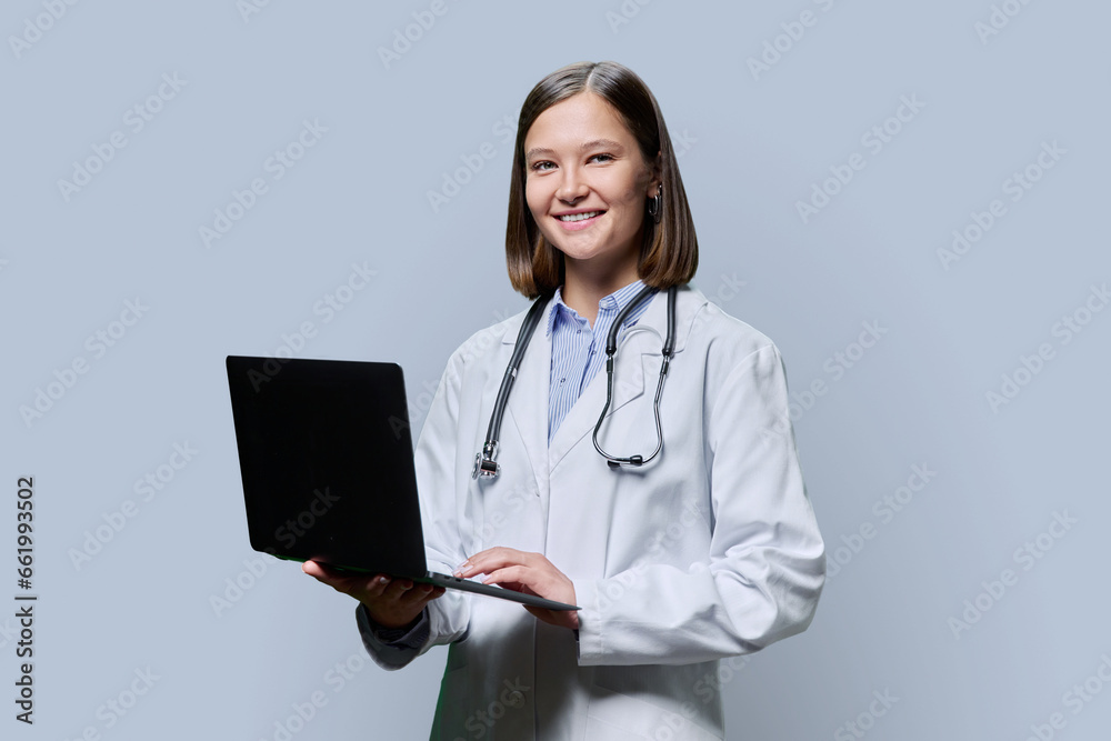 Young woman doctor, medical student with laptop on grey background Young woman doctor, medical student with laptop on grey background