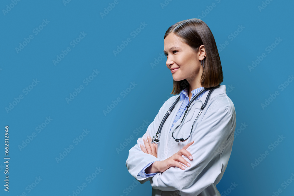 Young woman doctor looking in profile, copy space for advertising text image, blue background Young woman doctor looking in profile, copy space for advertising text image, blue background