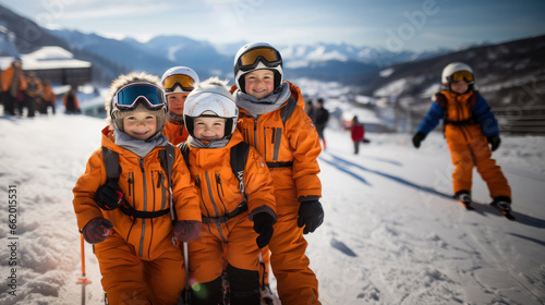 Group of children wear orange uniform skiing in the mountains on a sunny winter day.