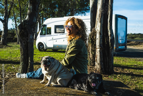 One woman sitting on the ground with her two best friends dogs pug in travel stop with alternative house vanlife motorhome camper in background. People and animals owner love concept. Outdoor leisure photo