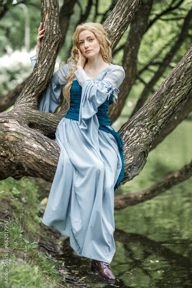 A young beautiful girl in a summer park. A beautiful medieval elf princess in a blue dress in the forest.