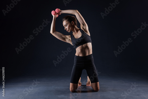 athletic girl in white clothes with dumbbells, on a dark background