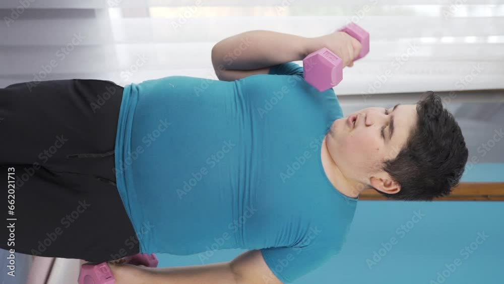 Vertical Video of Obesity boy working out weights with dumbbells in front of the glass. Vertical Video of Obesity boy working out weights with dumbbells in front of the glass.