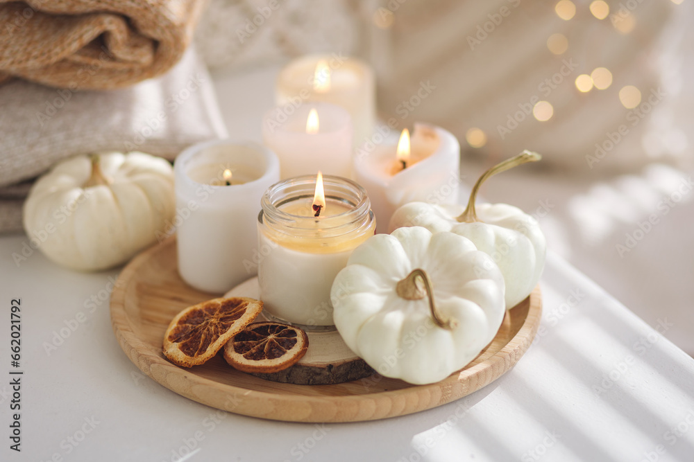 Autumn home decor with white pumpkins and burning aroma candles with sweet spicy pumpkin pie scent. Cozy fall composition, relaxation, aromatherapy. Apartment design, living room or bedroom