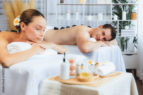 Hot stone massage at spa salon in luxury resort with day light serenity ambient, blissful couple customer enjoying spa basalt stone massage glide over body with soothing warmth. Quiescent